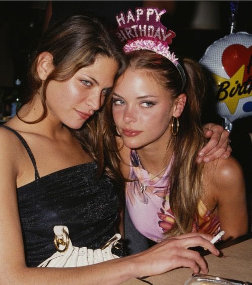 two young women sitting next to each other at a table with balloons in the background