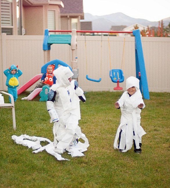 two children in white costumes playing with paper machs on the grass near a playground