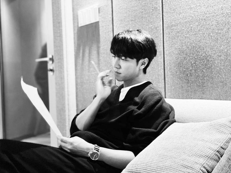 a young man sitting on top of a couch next to a wall holding a piece of paper