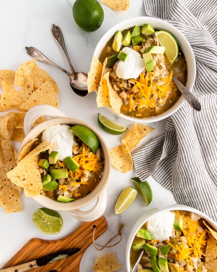 two bowls of chicken tortilla soup with sour cream and avocado on the side