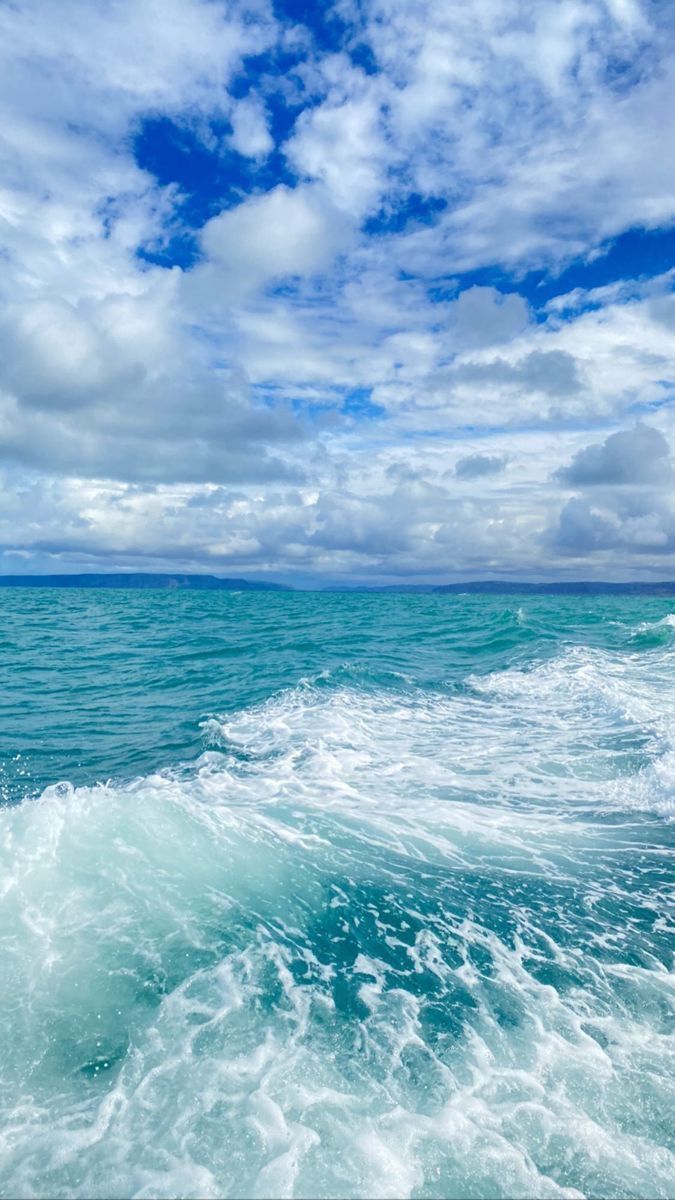 the ocean is blue and green with white clouds in the sky above it, as well as waves on the water