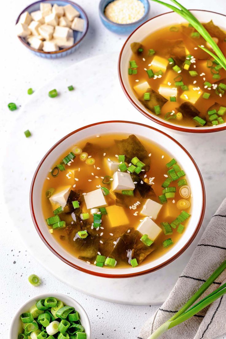 two bowls filled with soup on top of a white table next to some green onions