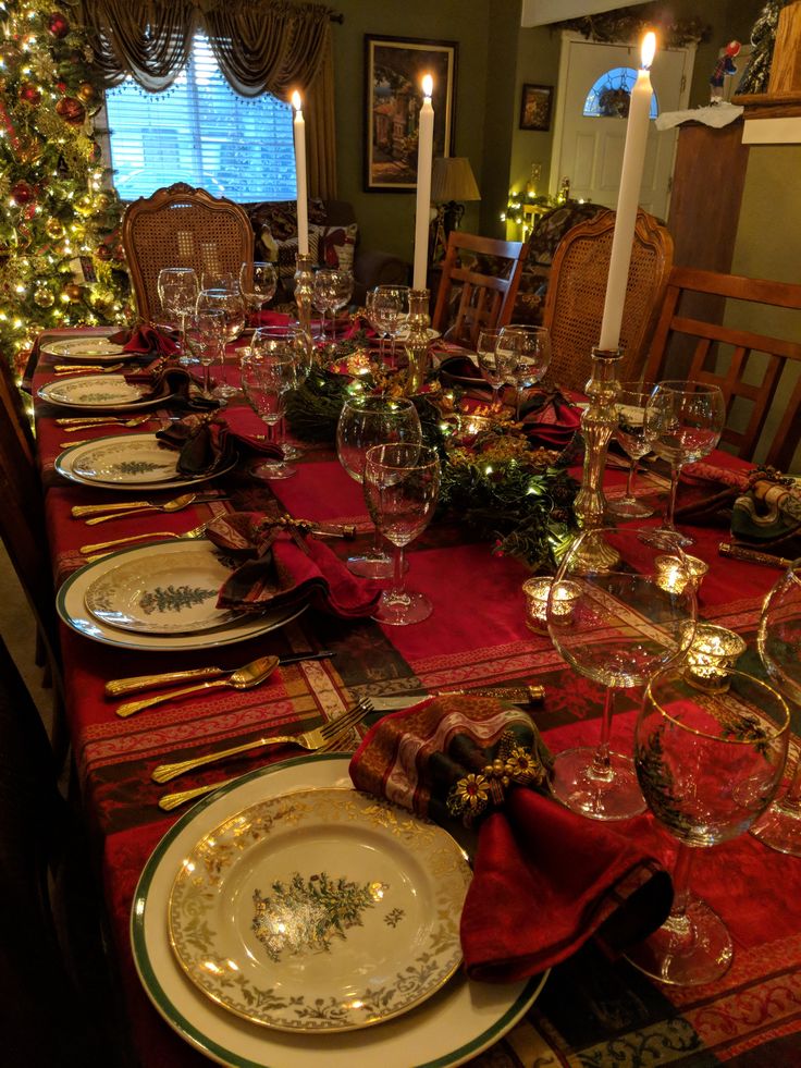 a dining room table set for christmas dinner with candles and place settings on the table