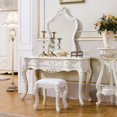 a white dressing table with two stools and a mirror on the wall behind it