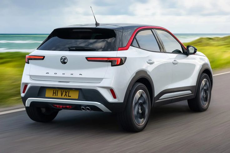 the rear end of a white opel suv driving down a road near the ocean