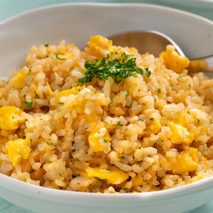 a white bowl filled with yellow rice and garnished with parsley on top