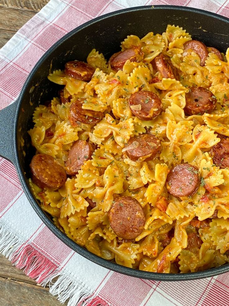 a skillet filled with pasta and sausage on top of a checkered table cloth