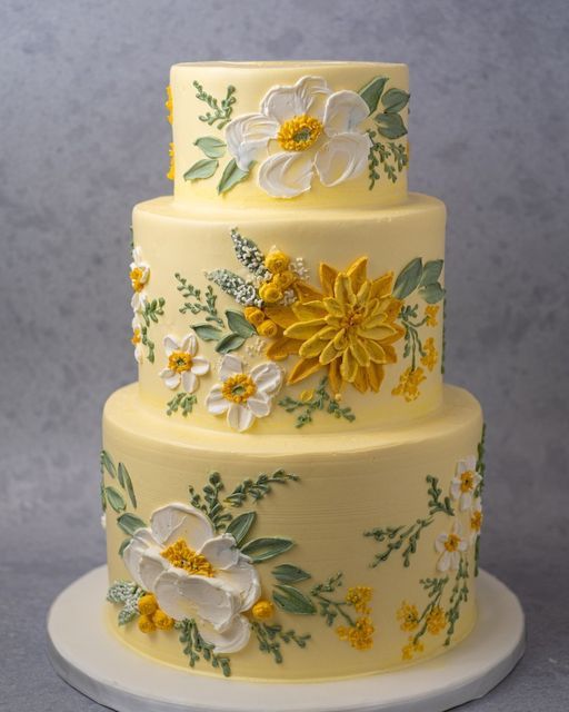 a three tiered cake decorated with yellow and white flowers