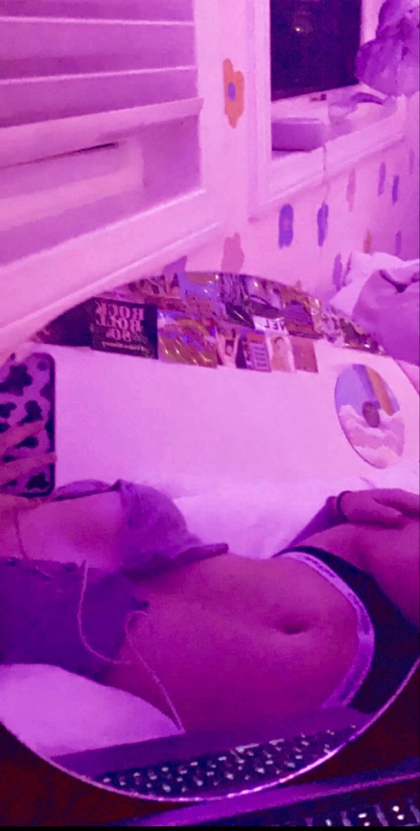 a woman laying on her stomach in front of a window with purple light coming through the blinds