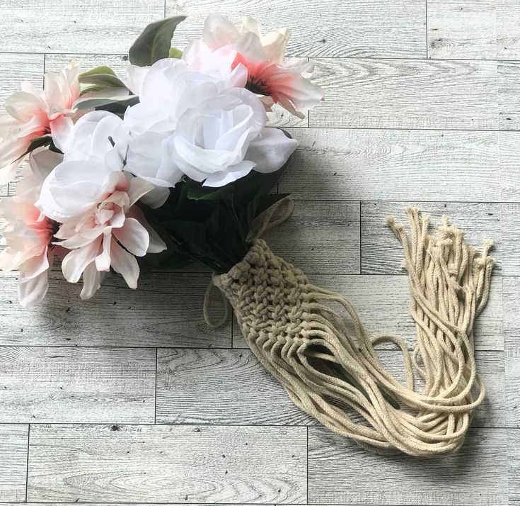 a bouquet of white and pink flowers sitting on top of a wooden floor next to a rope