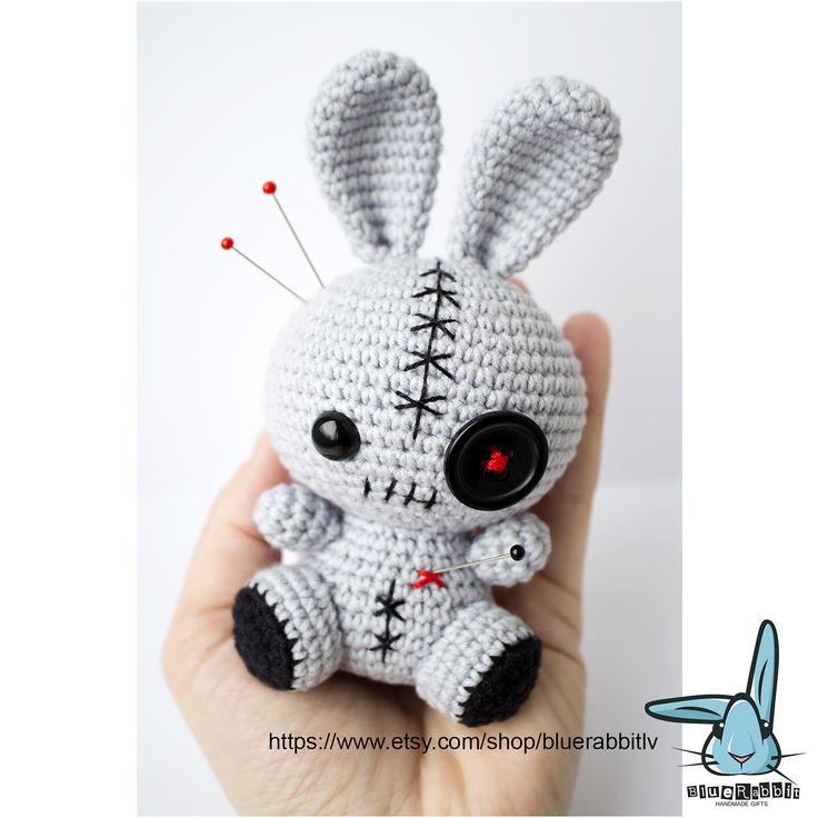 a small crocheted bunny with black eyes is held up by someone's hand