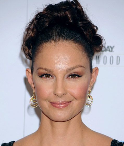 a woman in a black dress smiling and wearing large gold hoop earrings on her head