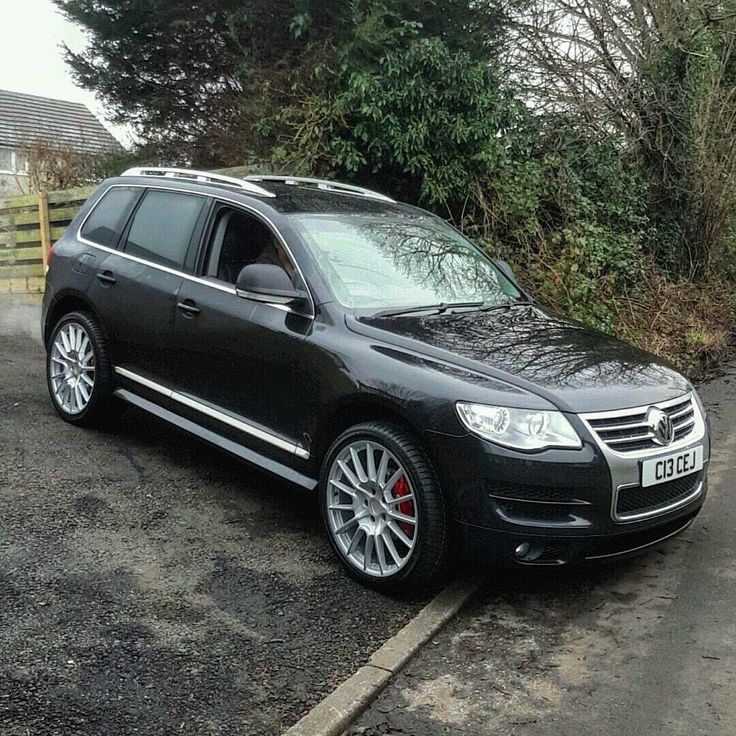 a black car parked on the side of a road next to a fence and trees