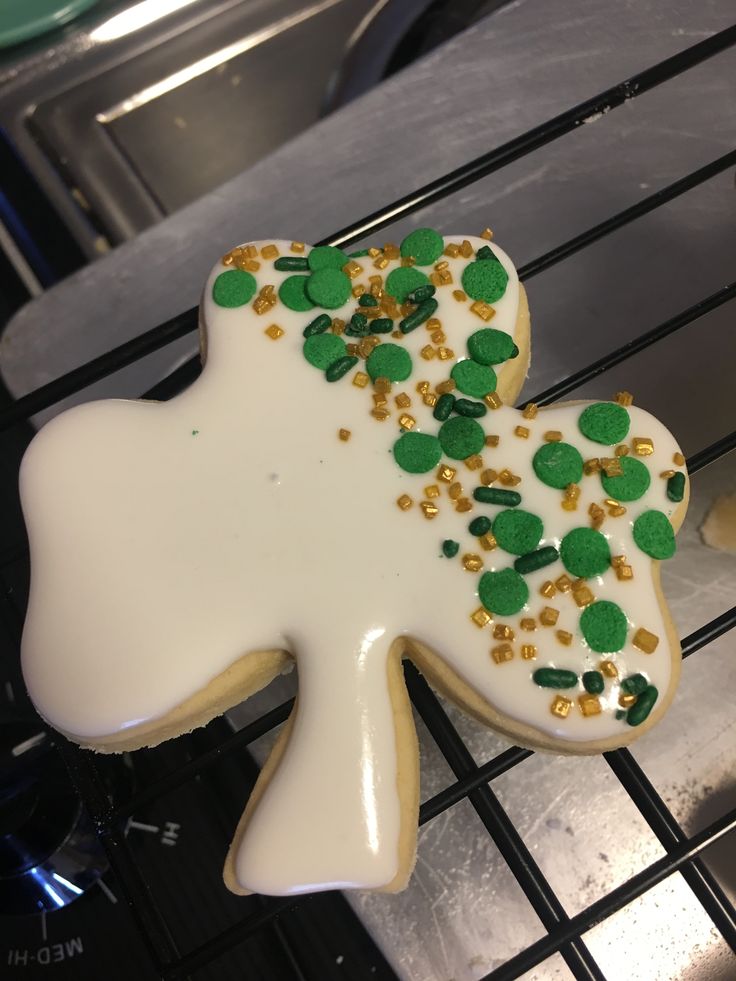 a decorated cookie with green and gold sprinkles sitting on a cooling rack