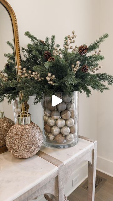 a vase filled with pine cones and balls on top of a table next to a mirror