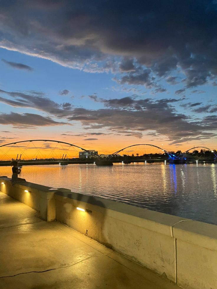 the sun is setting over the water and some lights are lit up in front of it