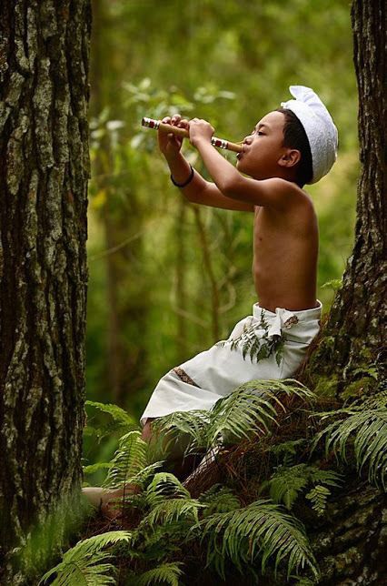 a young boy is sitting in the woods and drinking from a pipe with words written on it