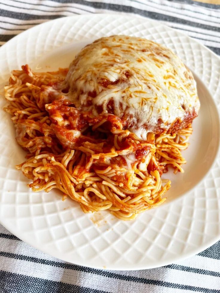 a white plate topped with spaghetti and meat covered in sauce on top of a checkered table cloth