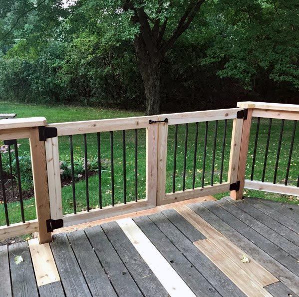 a wooden deck with metal railings in front of a green yard and trees on the other side