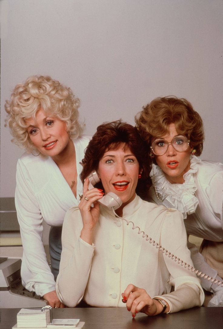 three women sitting at a table talking on the phone and one is holding a cellphone to her ear