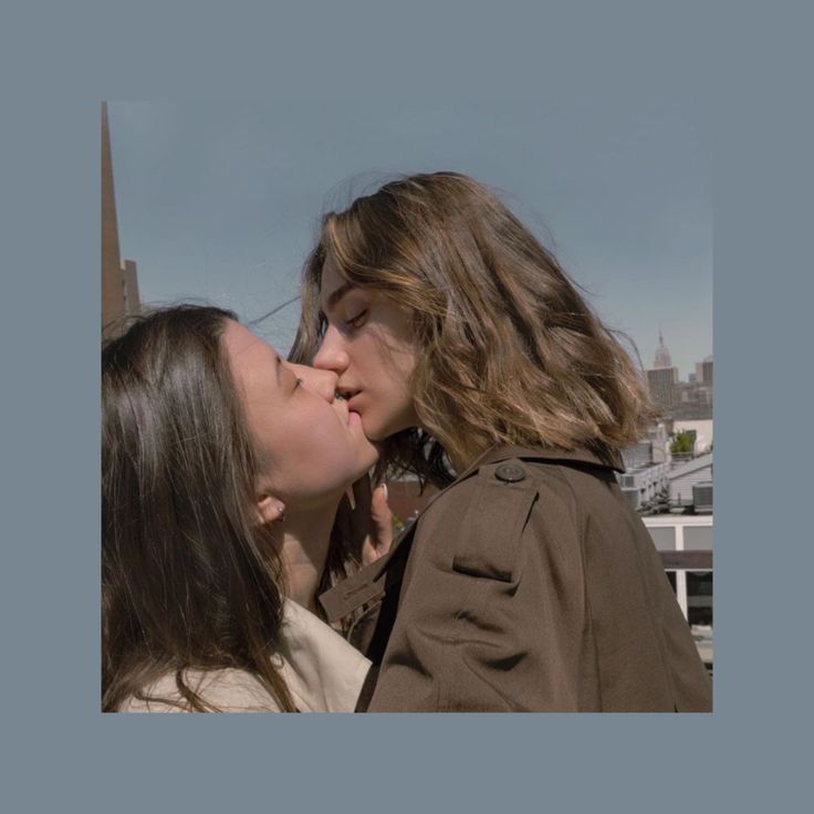 two young women kissing each other on top of a building