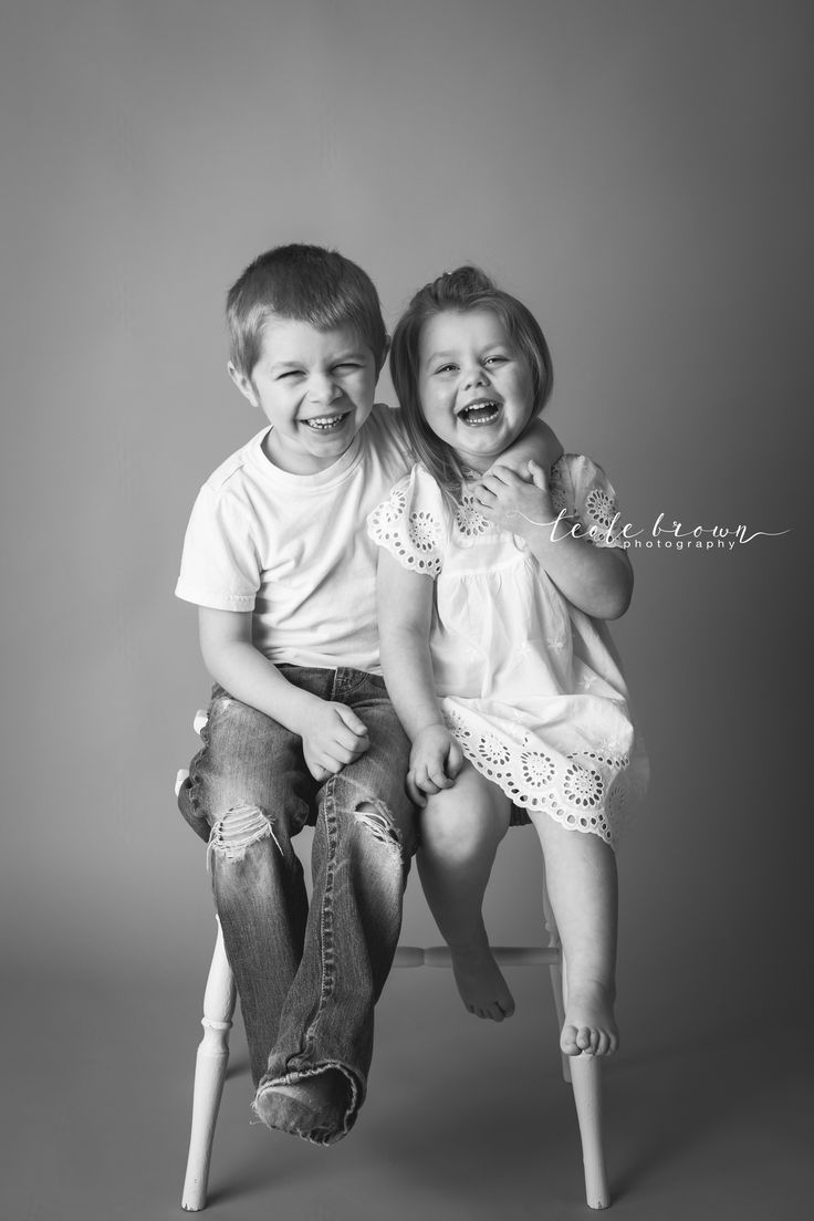 two young children sitting on top of each other in front of a gray background, smiling at the camera