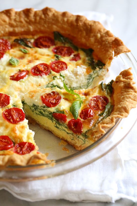 a quiche with tomatoes and spinach is on a glass plate, ready to be eaten