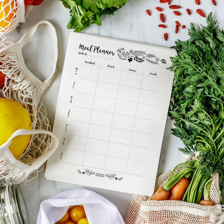 a meal planner surrounded by fruits and vegetables on a white marble counter top with grocery bags