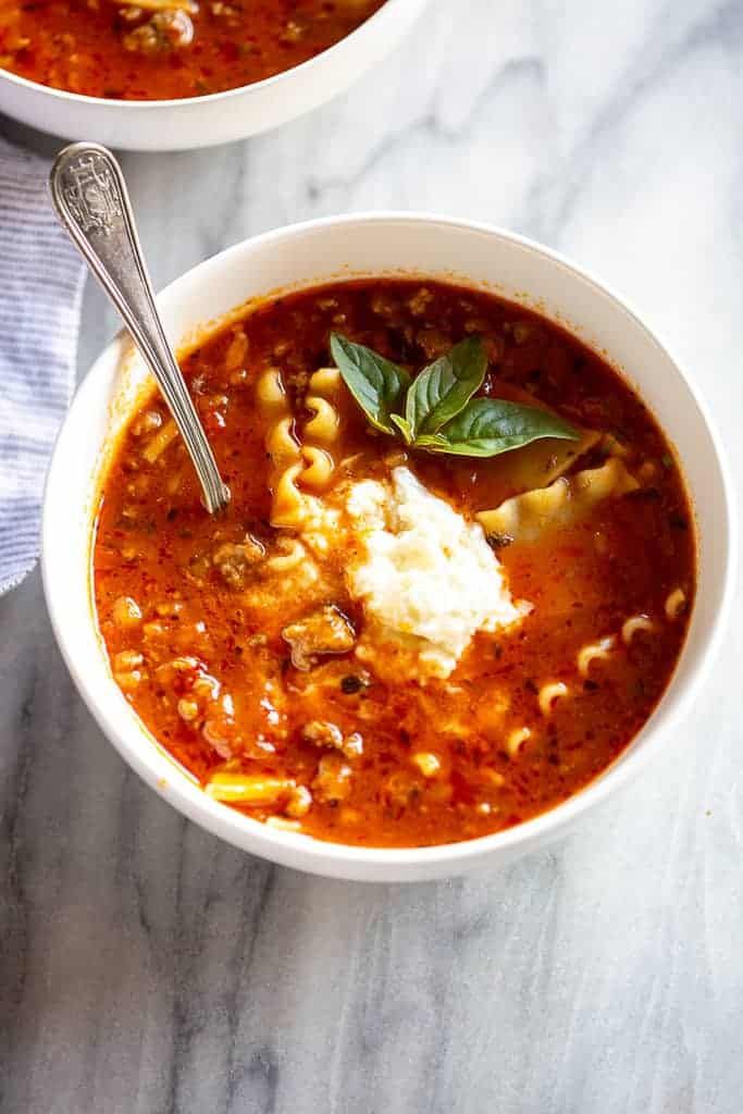 two bowls of pasta soup on a marble countertop with silver spoons and napkin