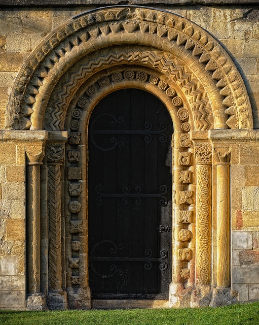 an arched doorway with decorative carvings on the side of a stone wall and green grass in front of it