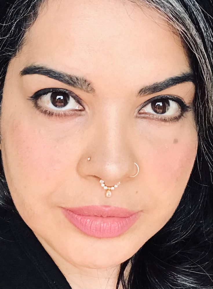 a woman with black hair wearing a nose ring and piercing on her nose is looking at the camera