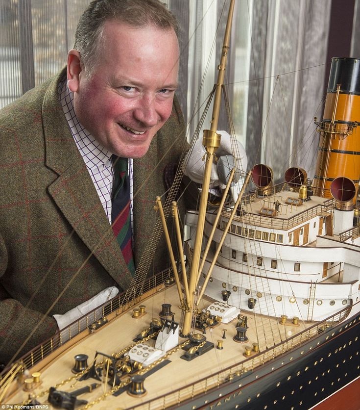 a man in a suit and tie standing next to a model ship