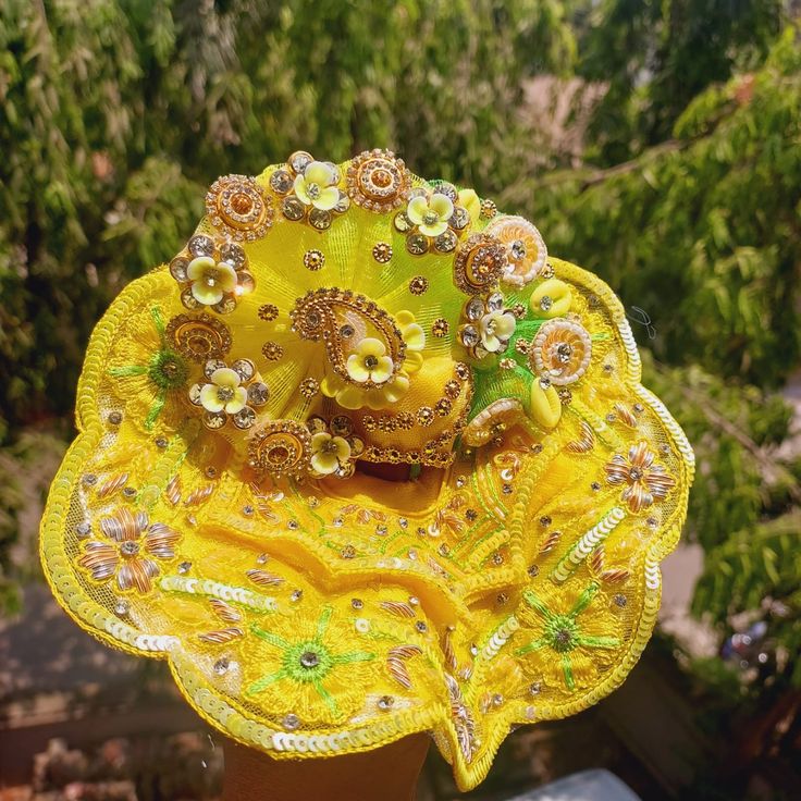 a close up of a yellow hat with flowers on it's side and trees in the background