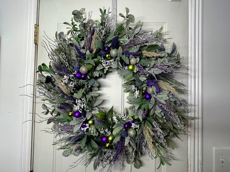 a wreath is hanging on the door with purple and green ornaments around it's edges