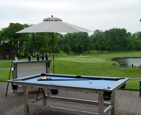 a pool table with an umbrella over it in front of a golf course on a cloudy day