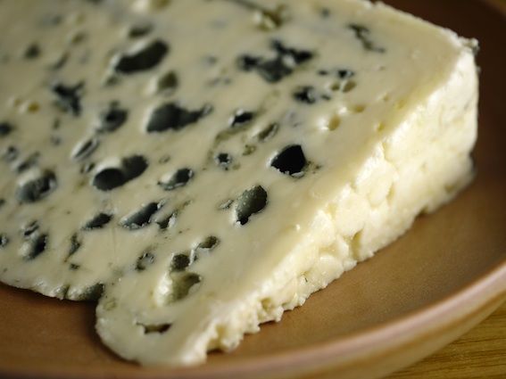 a piece of cheese on a plate with black olives and parmesan cheese