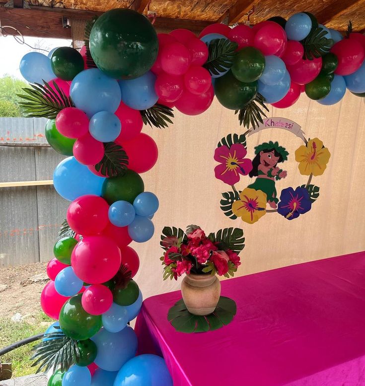 a table topped with balloons and flowers under a tent covered in pink, blue, and green