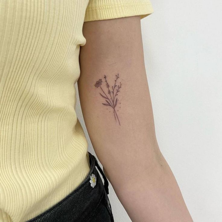 a woman's arm with a small flower tattoo on the back of her left arm