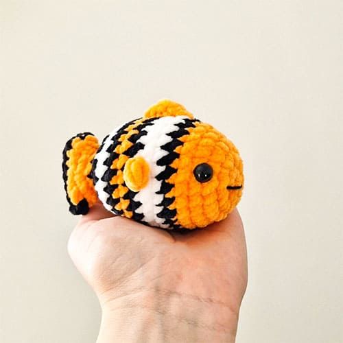 a hand holding a small orange and black stuffed animal with stripes on it's face