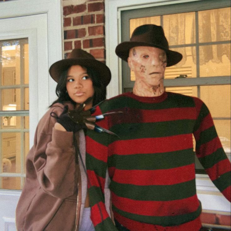 two people in costumes standing next to each other near a door with fake faces on them