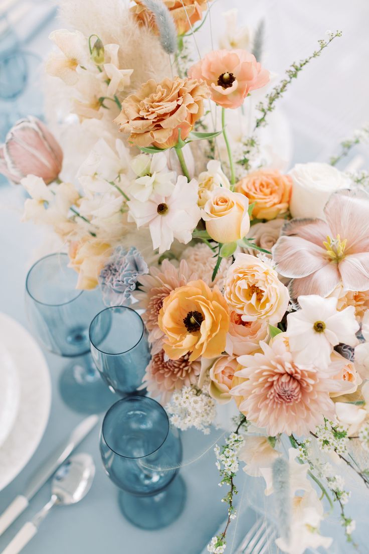 a vase filled with lots of flowers sitting on top of a blue table covered in white plates