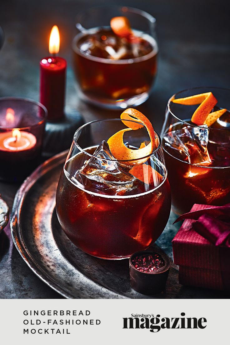 two glasses filled with liquid sitting on top of a table next to candles and napkins