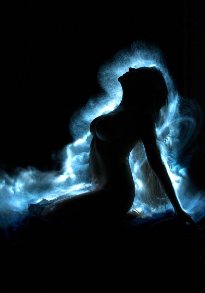 a woman sitting in the dark with blue fire behind her