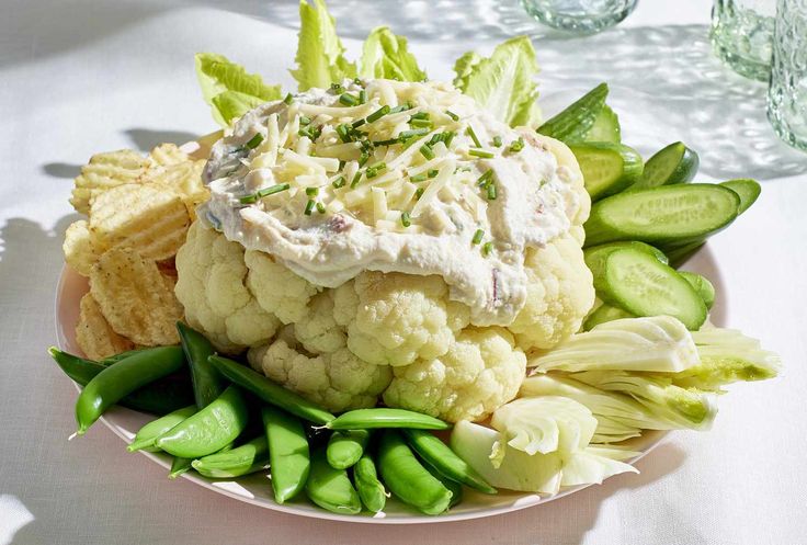 a white plate topped with cauliflower and cucumbers next to crackers