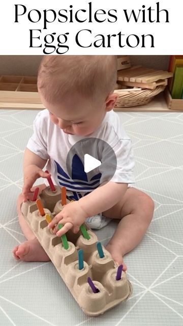 a baby sitting on the floor playing with an egg carton