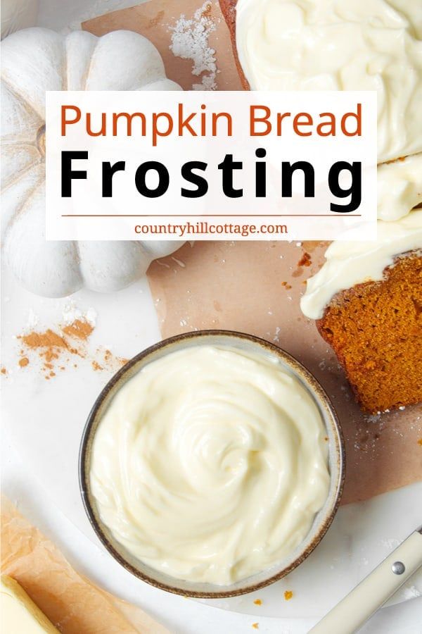 pumpkin bread frosted with white icing on a cutting board next to a cup of cream cheese