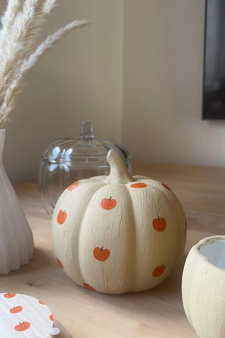 some pumpkins are sitting on a table next to a vase and other items in the background