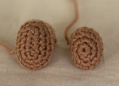 there are two crocheted balls sitting on the table together, one is brown and the other is beige