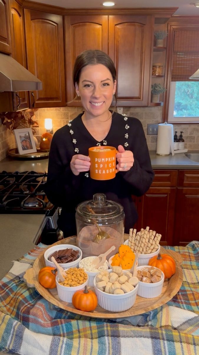 a woman holding a cup in her hands while standing next to a platter of food