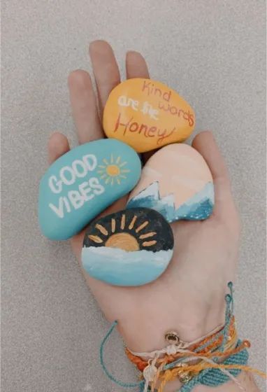 a hand holding three painted rocks that say good vibes